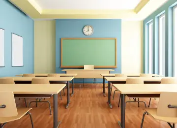 Empty classroom with desks, chairs, a green chalkboard, and a clock on the wall. Large windows on the right side let in natural light, while Hoya Ondol Heating Panels ensure a cozy atmosphere during colder months. - Hoya Ondol Aust