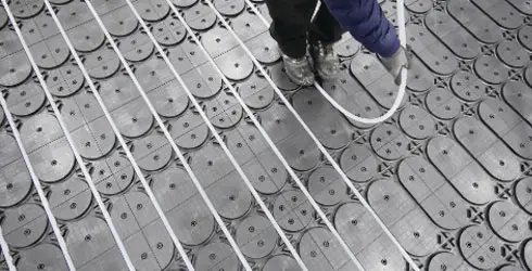 Person installing Hoya Ondol underfloor heating pipes on a grid pattern surface using the install method B panel. - Hoya Ondol Aust